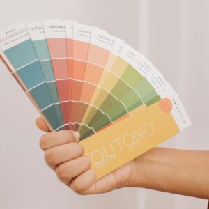 Hand holding a vibrant paint swatch fan against a curtain backdrop.