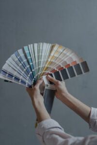 Hands holding color swatch samples in a fan shape against a gray background.